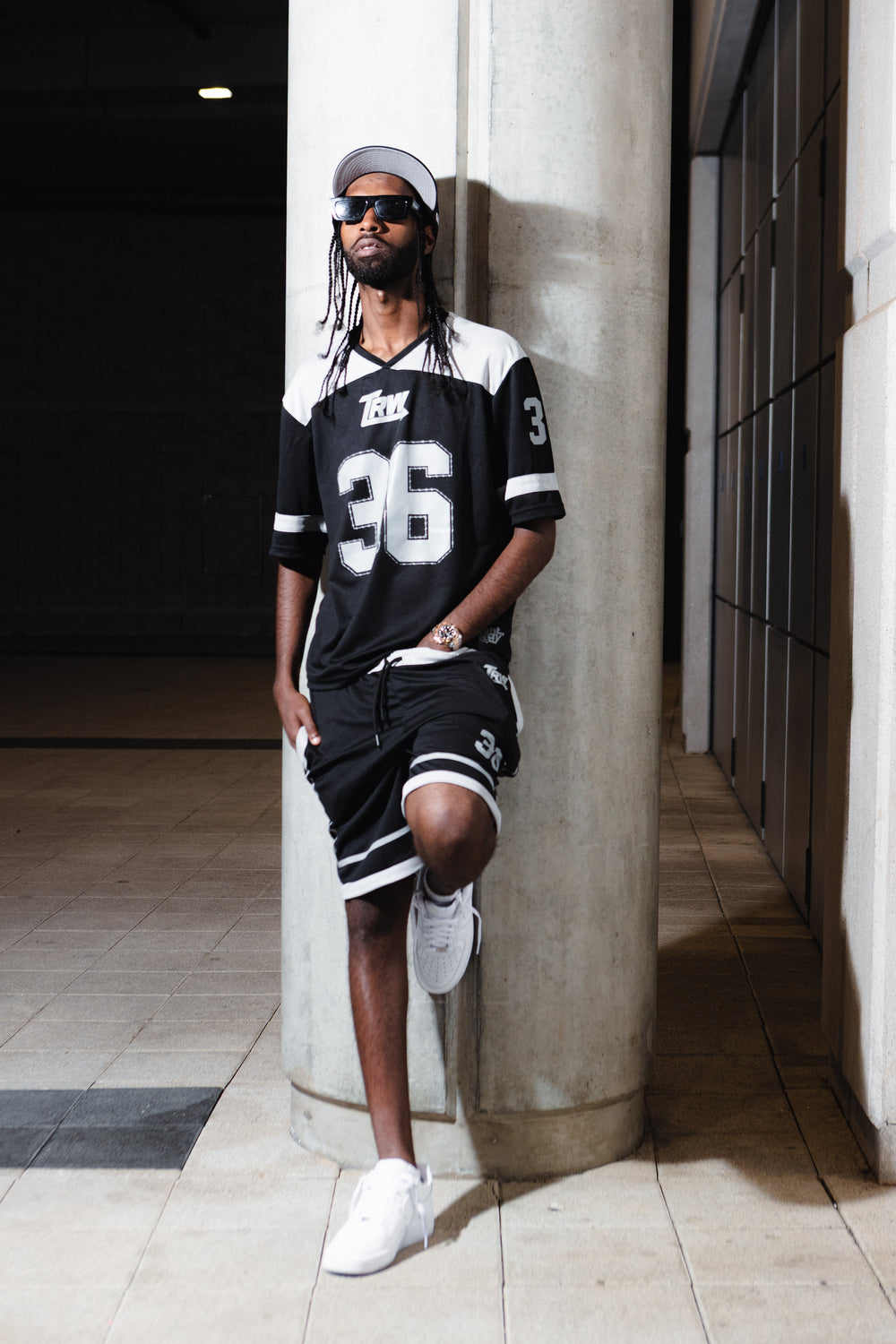 Model in the black TRW jersey set leaning against a concrete column